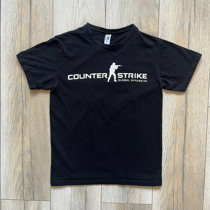 CS:GO Black &amp; White Logo 2010's Tee is a black T-shirt made on a JHK blank. The front features a large white CS:GO logo with an armed figure&nbsp; and “Counter-Strike Global Offensive” text below. Super simple - classic CS logo.