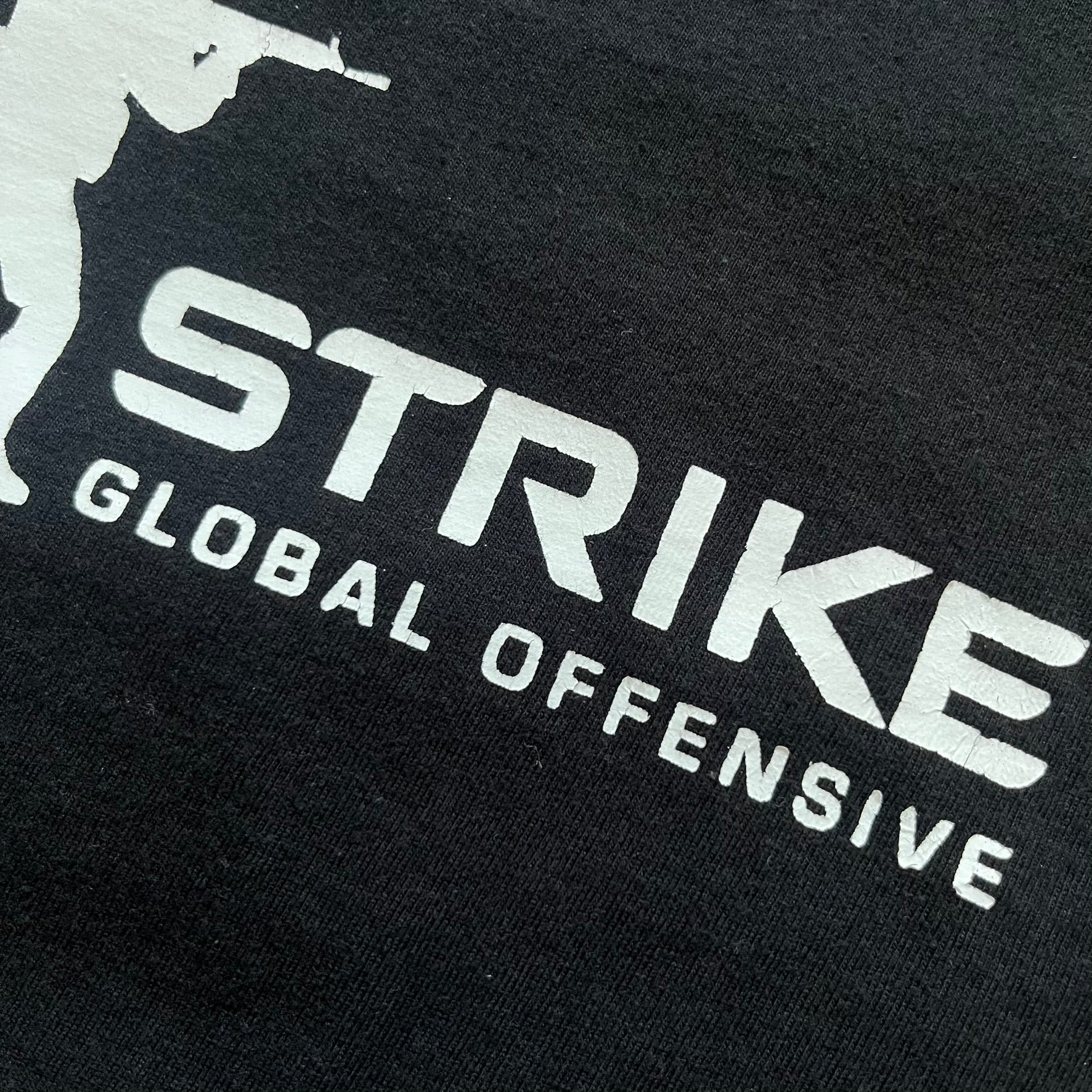 CS:GO Black &amp; White Logo 2010's Tee is a black T-shirt made on a JHK blank. The front features a large white CS:GO logo with an armed figure&nbsp; and “Counter-Strike Global Offensive” text below. Super simple - classic CS logo.