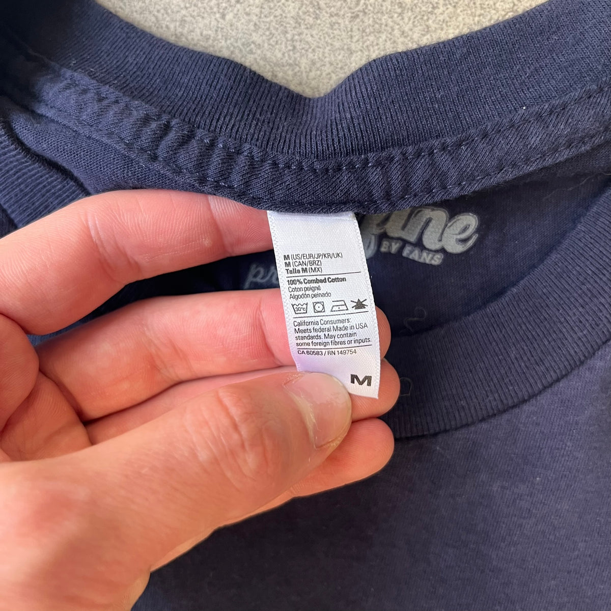 CS:GO Easy Peasy Lemon Squeezy 2015 Tee is a navy T-shirt made in the USA by We Love Fine, featuring a large CS:GO sticker graphic on the front of a hand squeezing a lemon with “Easy Peasy Lemon Squeezy” text. A CS:GO logo is printed on the back below the collar, and it carries a licensed 2015 tag.