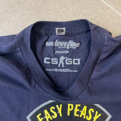 CS:GO Easy Peasy Lemon Squeezy 2015 Tee is a navy T-shirt made in the USA by We Love Fine, featuring a large CS:GO sticker graphic on the front of a hand squeezing a lemon with “Easy Peasy Lemon Squeezy” text. A CS:GO logo is printed on the back below the collar, and it carries a licensed 2015 tag.