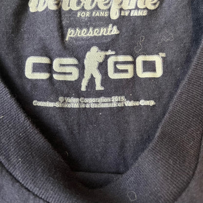 CS:GO Easy Peasy Lemon Squeezy 2015 Tee is a navy T-shirt made in the USA by We Love Fine, featuring a large CS:GO sticker graphic on the front of a hand squeezing a lemon with “Easy Peasy Lemon Squeezy” text. A CS:GO logo is printed on the back below the collar, and it carries a licensed 2015 tag.