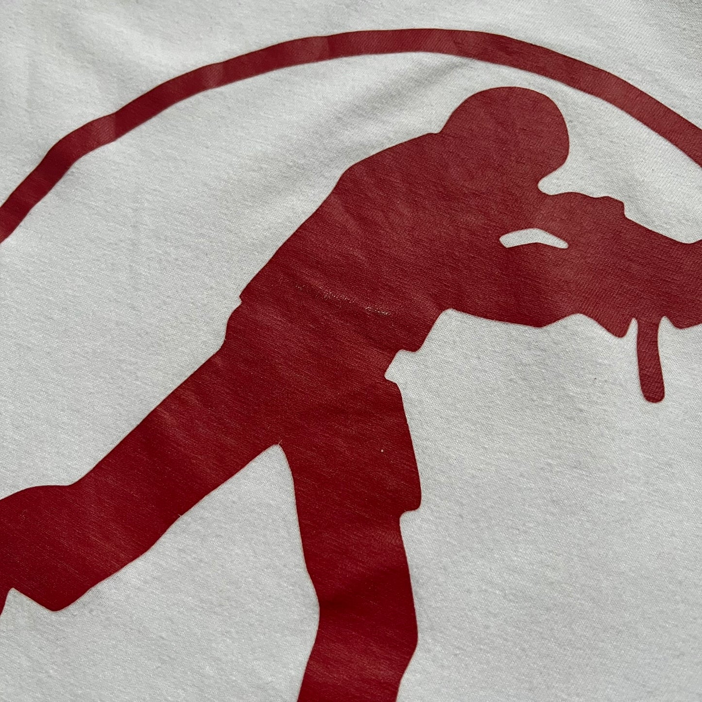 CS:GO White & Red Logo 2010’s Tee is a white T-shirt made from 100% cotton on a Gildan blank. The front features a large red CS:GO logo with an armed figure inside a circle and “Counter-Strike Global Offensive” text below. The shirt reflects early 2010s CS:GO merchandise design.