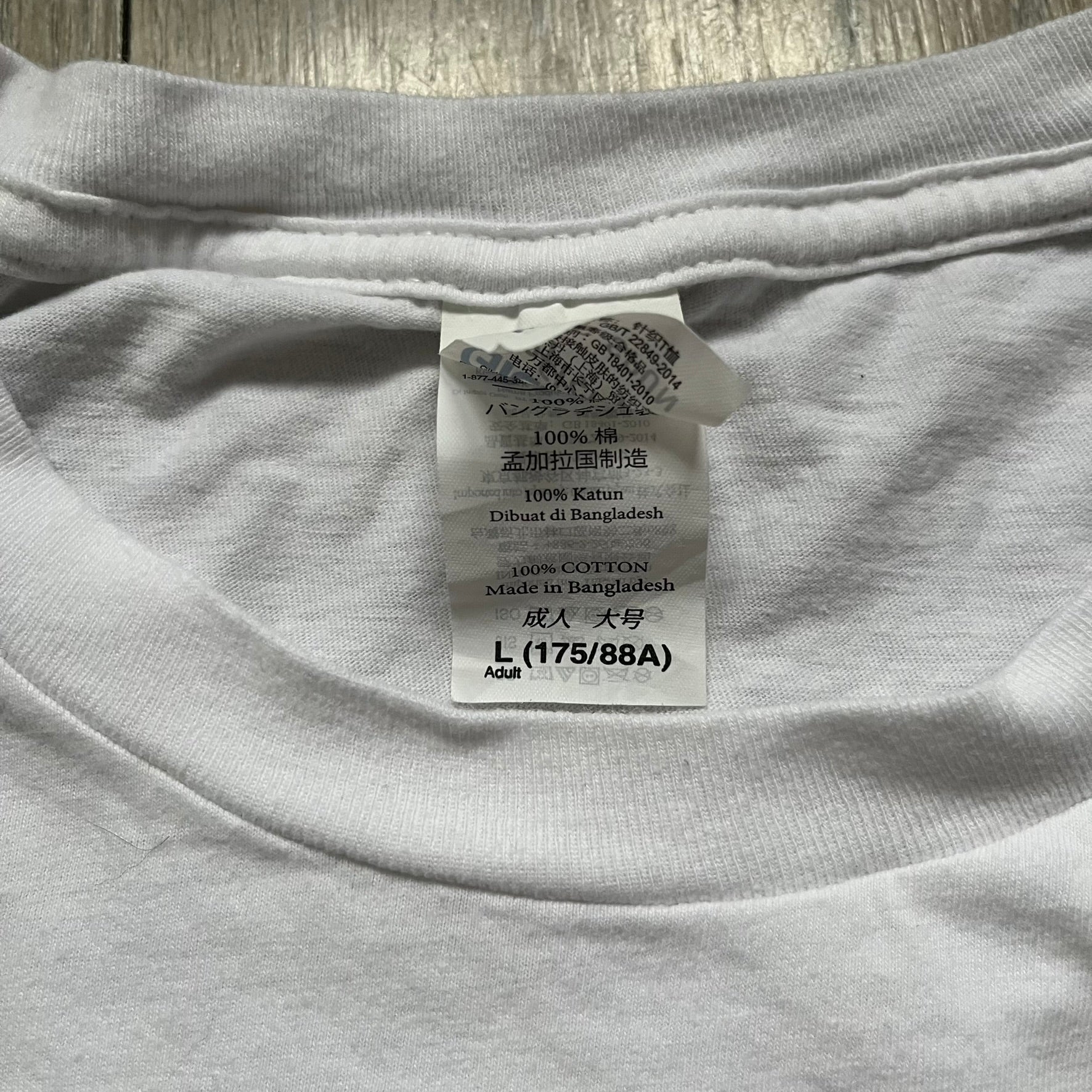 CS:GO White & Red Logo 2010’s Tee is a white T-shirt made from 100% cotton on a Gildan blank. The front features a large red CS:GO logo with an armed figure inside a circle and “Counter-Strike Global Offensive” text below. The shirt reflects early 2010s CS:GO merchandise design.