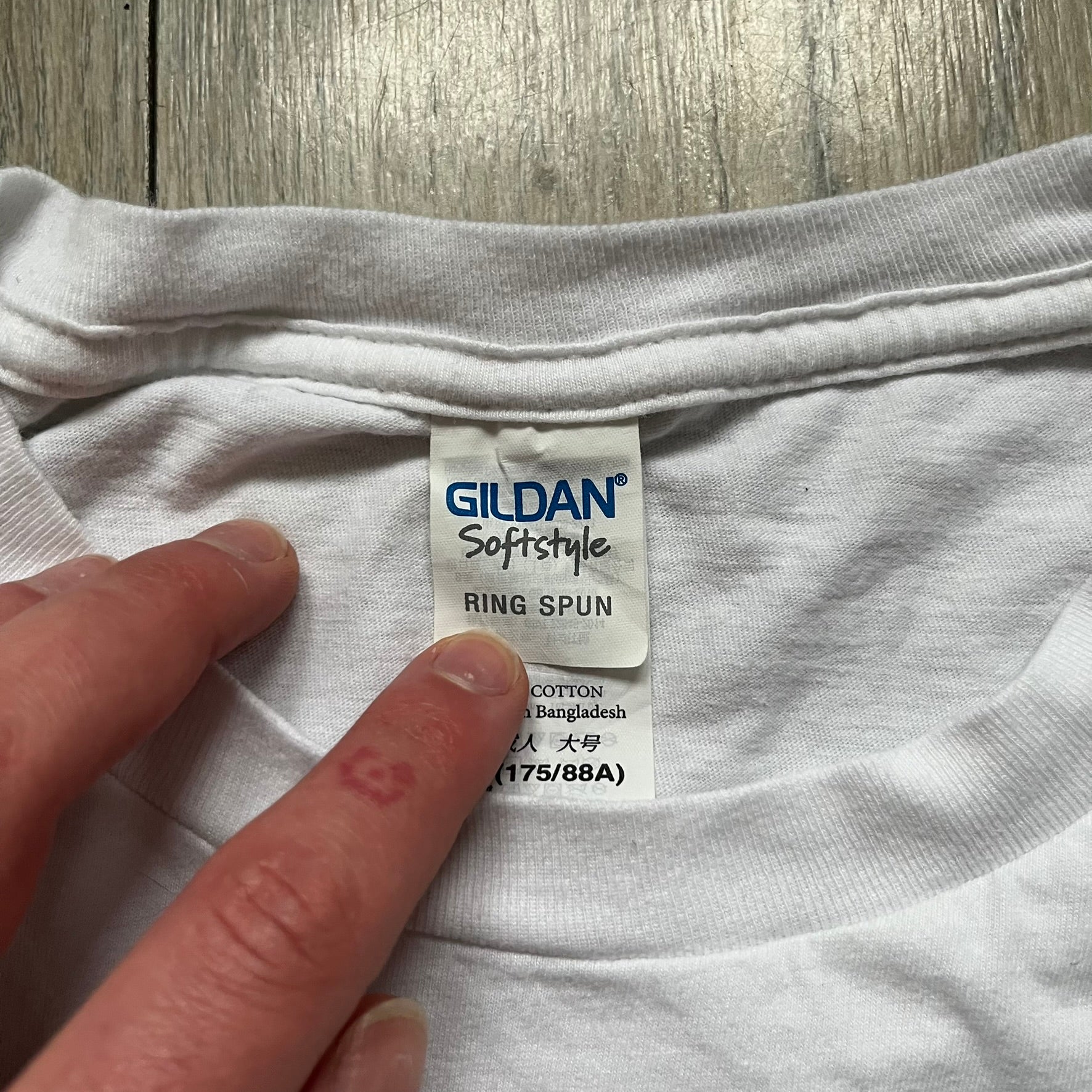 CS:GO White & Red Logo 2010’s Tee is a white T-shirt made from 100% cotton on a Gildan blank. The front features a large red CS:GO logo with an armed figure inside a circle and “Counter-Strike Global Offensive” text below. The shirt reflects early 2010s CS:GO merchandise design.