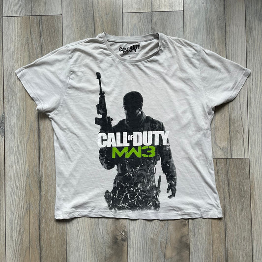 Call of Duty: MW3 2011 Cover Tee is a white to very light beige T-shirt featuring the Call of Duty: Modern Warfare 3 cover artwork printed on the front. The graphic includes the Call of Duty MW3 logo and the game's main cover image in black and gray tones. The shirt includes MW3 licensing on the neck tag.