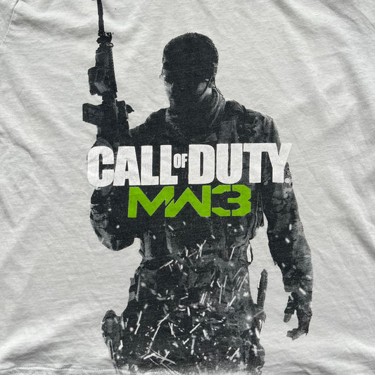 Call of Duty: MW3 2011 Cover Tee is a white to very light beige T-shirt featuring the Call of Duty: Modern Warfare 3 cover artwork printed on the front. The graphic includes the Call of Duty MW3 logo and the game's main cover image in black and gray tones. The shirt includes MW3 licensing on the neck tag.