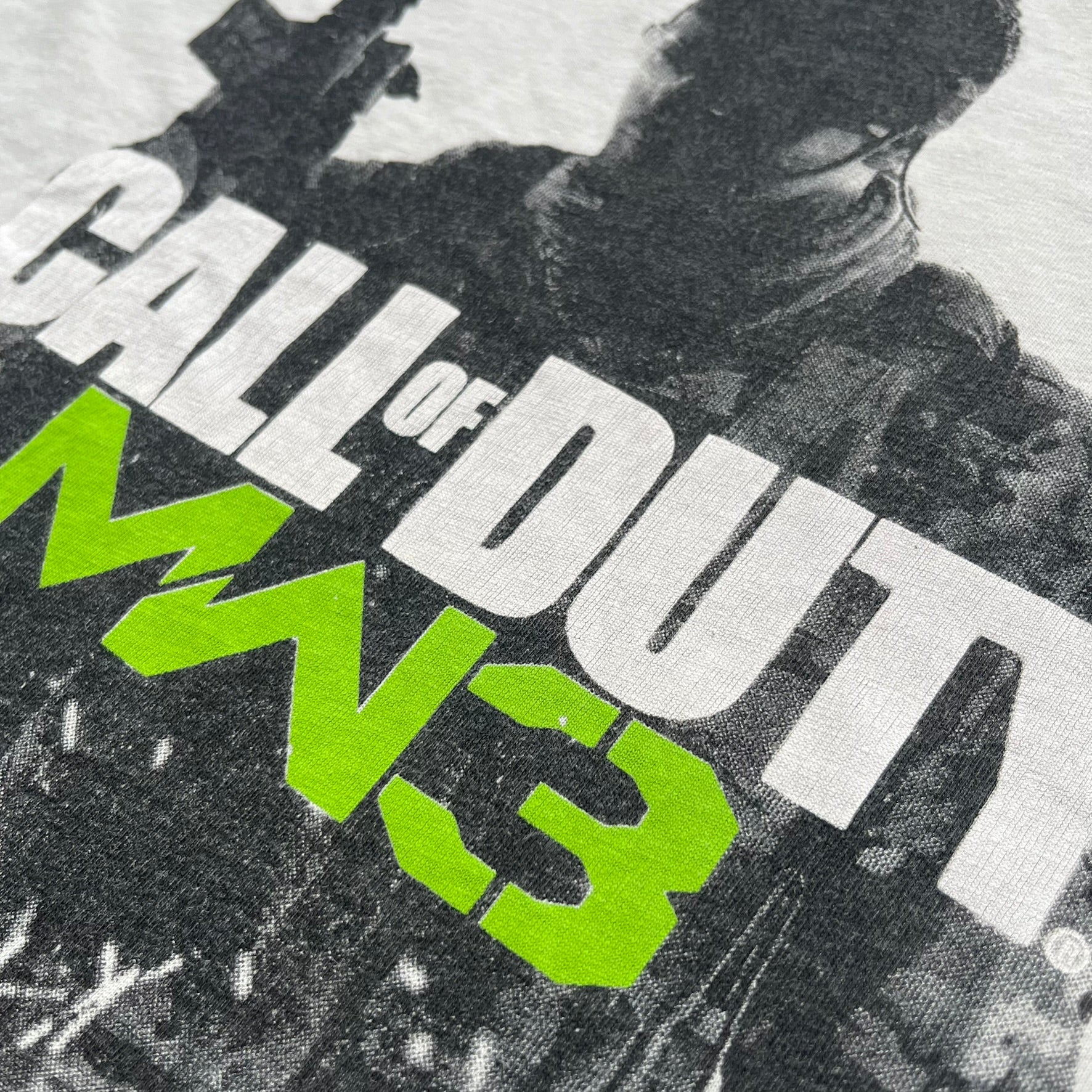 Call of Duty: MW3 2011 Cover Tee is a white to very light beige T-shirt featuring the Call of Duty: Modern Warfare 3 cover artwork printed on the front. The graphic includes the Call of Duty MW3 logo and the game's main cover image in black and gray tones. The shirt includes MW3 licensing on the neck tag.