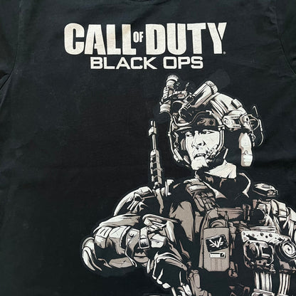 Call of Duty: Black Ops 2018 Black Tee is a black promotional T-shirt with a 2018 Activision Publishing licensed neck tag. The front features a large white and grey character graphic in armor holding a weapon, with the “Call of Duty Black Ops” logo printed above. The print spans most of the front from top to bottom.
