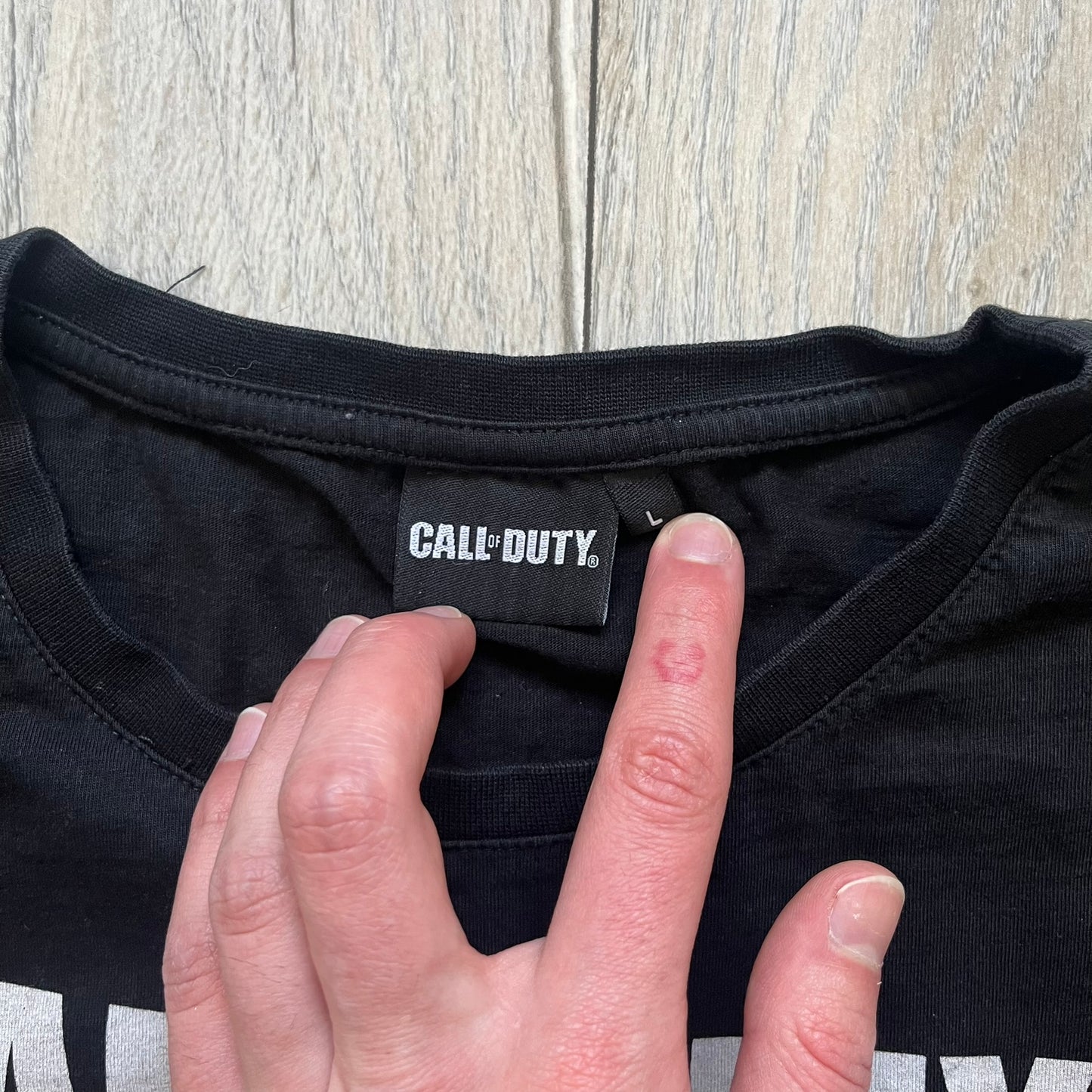 Call of Duty: Black Ops 2018 Black Tee is a black promotional T-shirt with a 2018 Activision Publishing licensed neck tag. The front features a large white and grey character graphic in armor holding a weapon, with the “Call of Duty Black Ops” logo printed above. The print spans most of the front from top to bottom.
