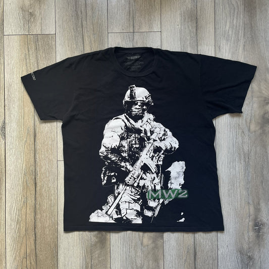 Call of Duty: Modern Warfare 2 2009 Tee is a black T-shirt featuring a large white detailed character with rifle print from the game, under it - green “MW2” text. The sleeve includes an Infinity Ward logo, and the neck tag shows 2009 Activision LVLP branding. Official merchandise from the 2009 Modern Warfare 2 release.