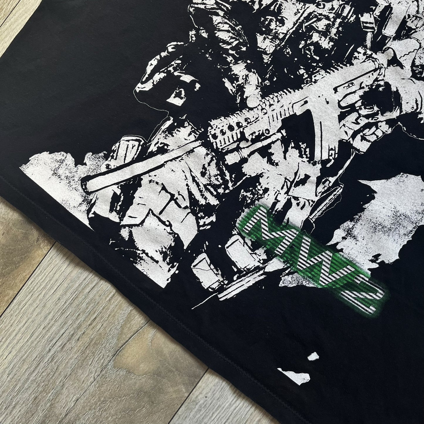 Call of Duty: Modern Warfare 2 2009 Tee is a black T-shirt featuring a large white detailed character with rifle print from the game, under it - green “MW2” text. The sleeve includes an Infinity Ward logo, and the neck tag shows 2009 Activision LVLP branding. Official merchandise from the 2009 Modern Warfare 2 release.