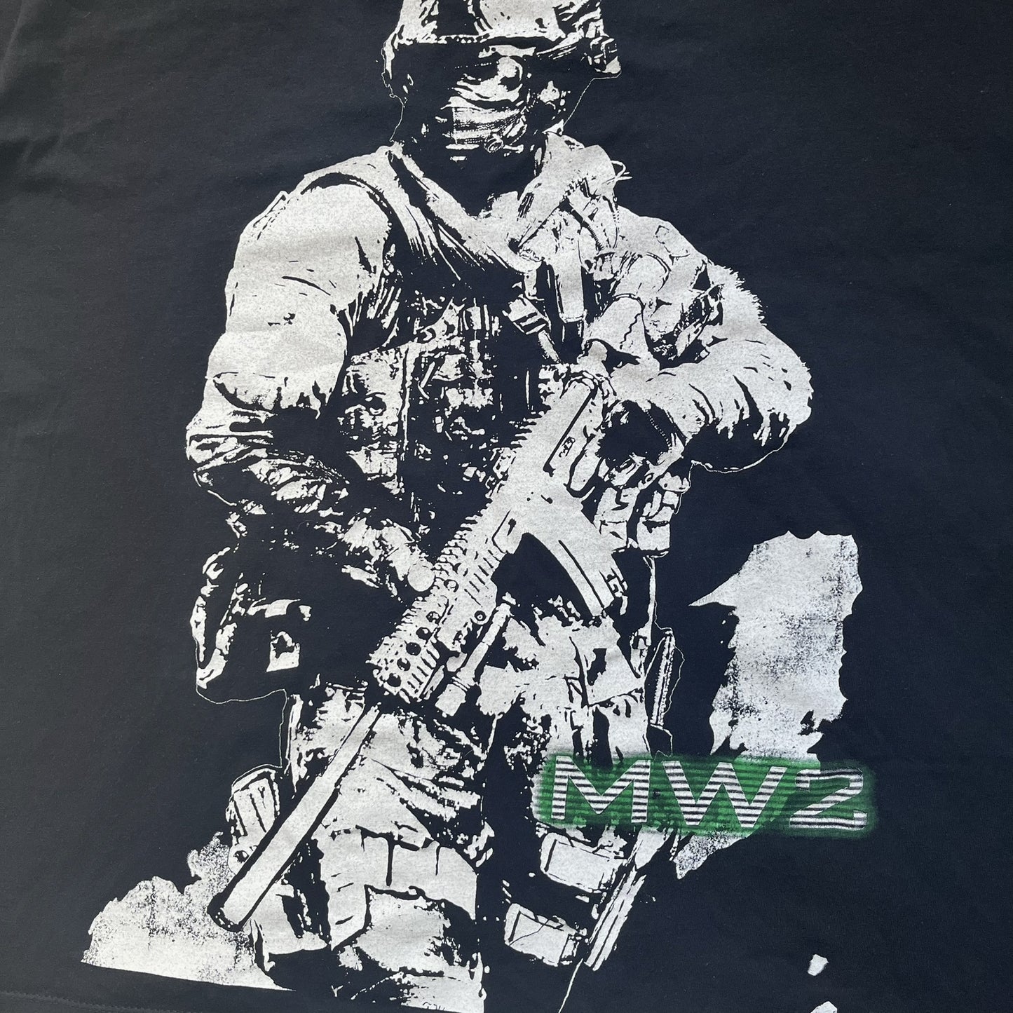 Call of Duty: Modern Warfare 2 2009 Tee is a black T-shirt featuring a large white detailed character with rifle print from the game, under it - green “MW2” text. The sleeve includes an Infinity Ward logo, and the neck tag shows 2009 Activision LVLP branding. Official merchandise from the 2009 Modern Warfare 2 release.
