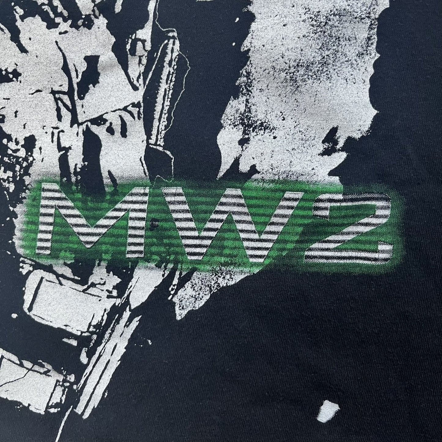 Call of Duty: Modern Warfare 2 2009 Tee is a black T-shirt featuring a large white detailed character with rifle print from the game, under it - green “MW2” text. The sleeve includes an Infinity Ward logo, and the neck tag shows 2009 Activision LVLP branding. Official merchandise from the 2009 Modern Warfare 2 release.