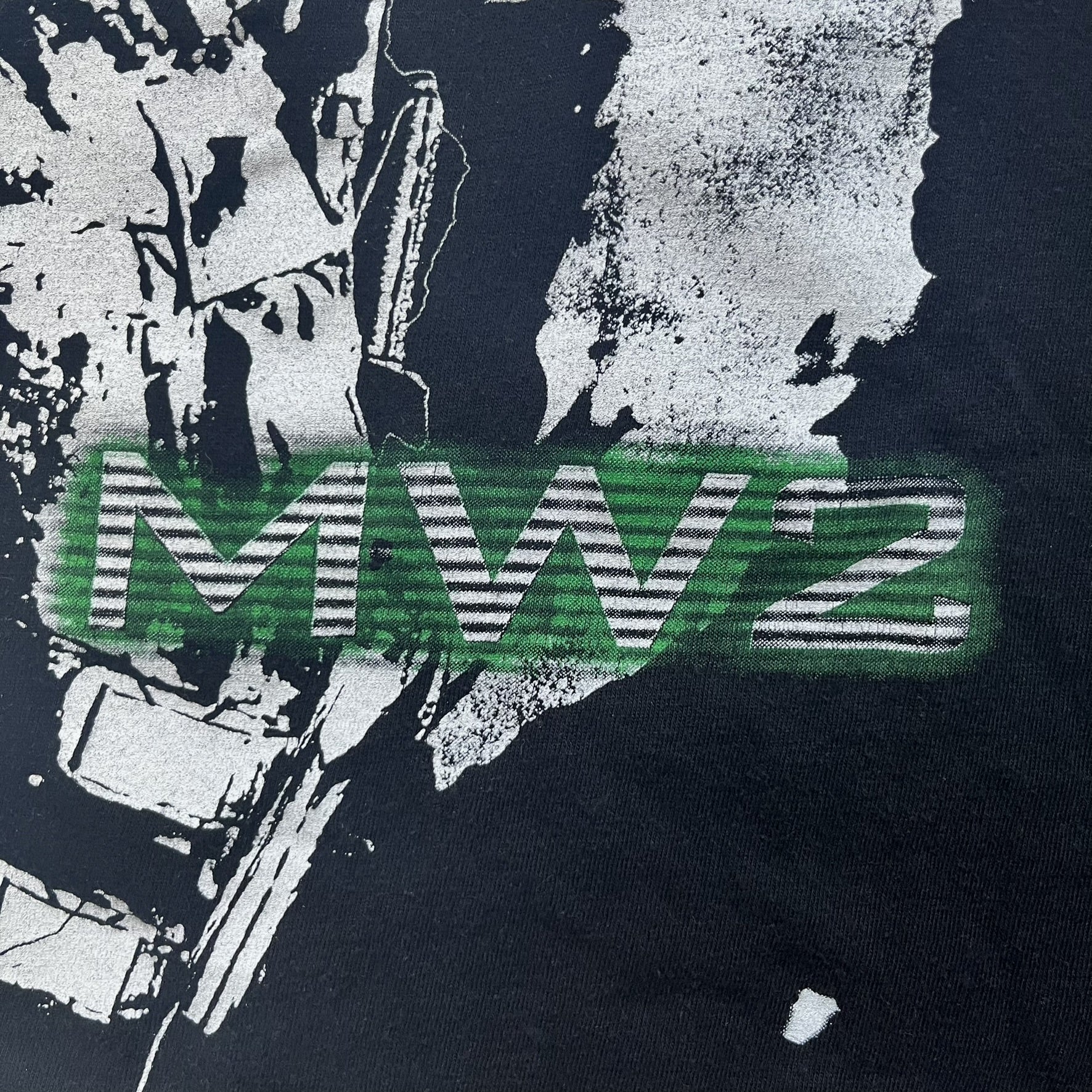 Call of Duty: Modern Warfare 2 2009 Tee is a black T-shirt featuring a large white detailed character with rifle print from the game, under it - green “MW2” text. The sleeve includes an Infinity Ward logo, and the neck tag shows 2009 Activision LVLP branding. Official merchandise from the 2009 Modern Warfare 2 release.