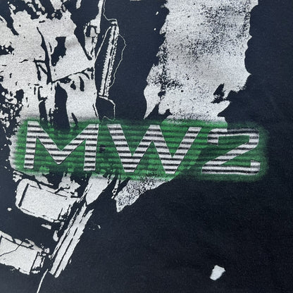 Call of Duty: Modern Warfare 2 2009 Tee is a black T-shirt featuring a large white detailed character with rifle print from the game, under it - green “MW2” text. The sleeve includes an Infinity Ward logo, and the neck tag shows 2009 Activision LVLP branding. Official merchandise from the 2009 Modern Warfare 2 release.