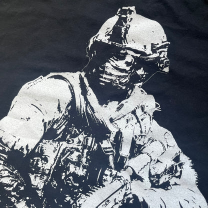 Call of Duty: Modern Warfare 2 2009 Tee is a black T-shirt featuring a large white detailed character with rifle print from the game, under it - green “MW2” text. The sleeve includes an Infinity Ward logo, and the neck tag shows 2009 Activision LVLP branding. Official merchandise from the 2009 Modern Warfare 2 release.