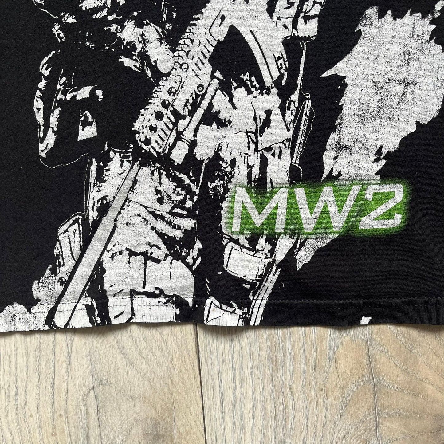 Call of Duty: Modern Warfare 2 2009 Tee is a black T-shirt featuring a large white detailed character print from the game with green “MW2” text below. The sleeve includes an Infinity Ward logo, and the neck tag shows 2009 Activision LVLP branding. Official merchandise from the 2009 Modern Warfare 2 release.