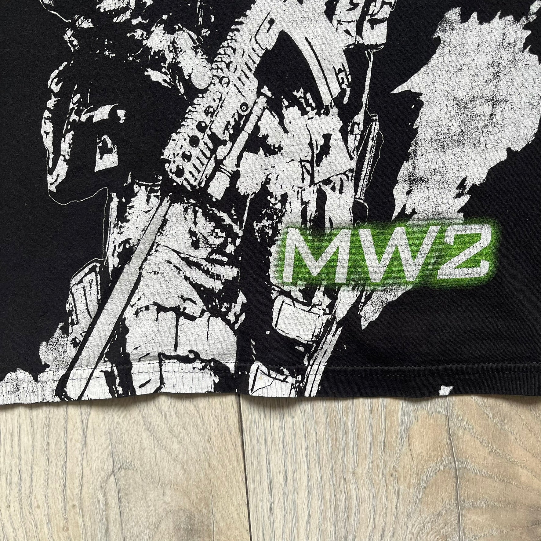 Call of Duty: Modern Warfare 2 2009 Tee is a black T-shirt featuring a large white detailed character print from the game with green “MW2” text below. The sleeve includes an Infinity Ward logo, and the neck tag shows 2009 Activision LVLP branding. Official merchandise from the 2009 Modern Warfare 2 release.