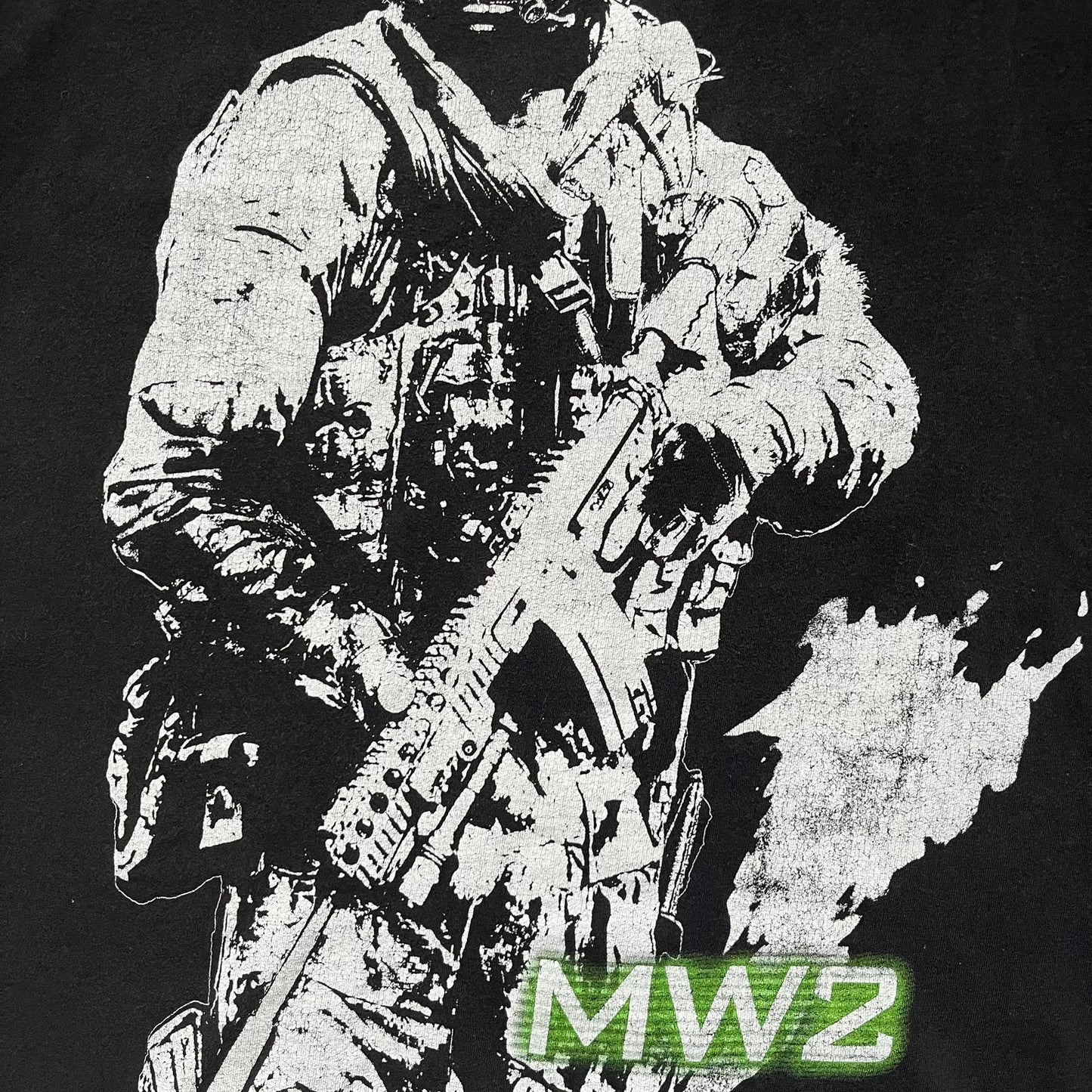 Call of Duty: Modern Warfare 2 2009 Tee is a black T-shirt featuring a large white detailed character print from the game with green “MW2” text below. The sleeve includes an Infinity Ward logo, and the neck tag shows 2009 Activision LVLP branding. Official merchandise from the 2009 Modern Warfare 2 release.