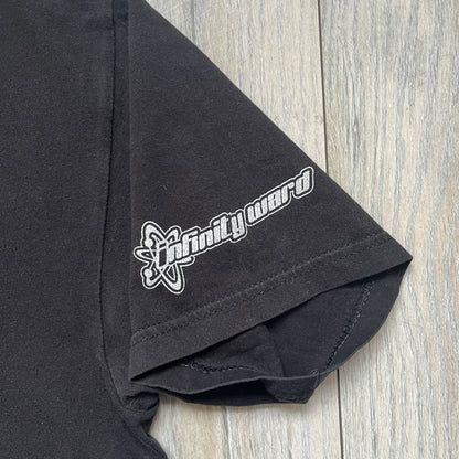 Call of Duty: Modern Warfare 2 2009 Tee is a black T-shirt featuring a large white detailed character print from the game with green “MW2” text below. The sleeve includes an Infinity Ward logo, and the neck tag shows 2009 Activision LVLP branding. Official merchandise from the 2009 Modern Warfare 2 release.