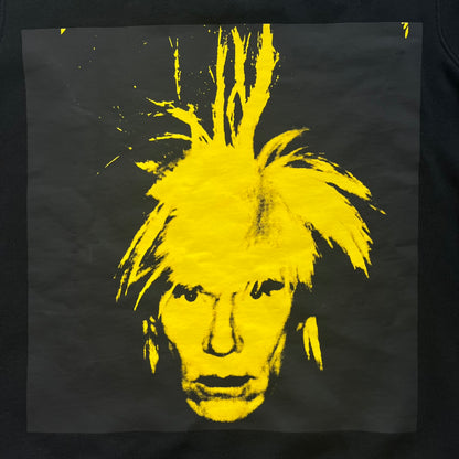 Calvin Klein x Andy Warhol 2018 Self-Portrait Crewneck is a black sweatshirt from the Calvin Klein Jeans x Andy Warhol collaboration. The front features a large yellow self-portrait graphic of Andy Warhol printed on a black background. It includes a yellow Calvin Klein Jeans x Andy Warhol neck tag and a collaboration patch near the bottom hem.
