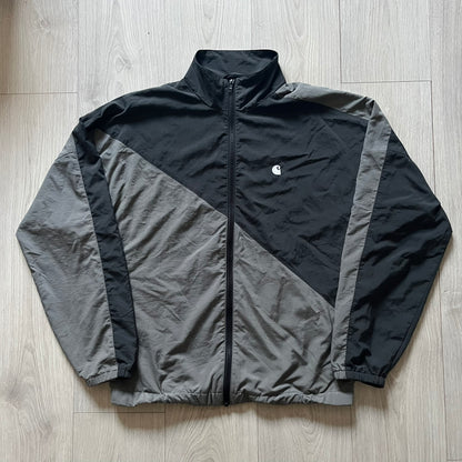 Carhartt WIP Gray Field Windbreaker featuring a dynamic two-tone design split diagonally across the body in light and dark gray. Crafted from durable nylon and polyester layers, it includes a small white Carhartt logo on the chest and large diagonal Carhartt embroidery on the back.