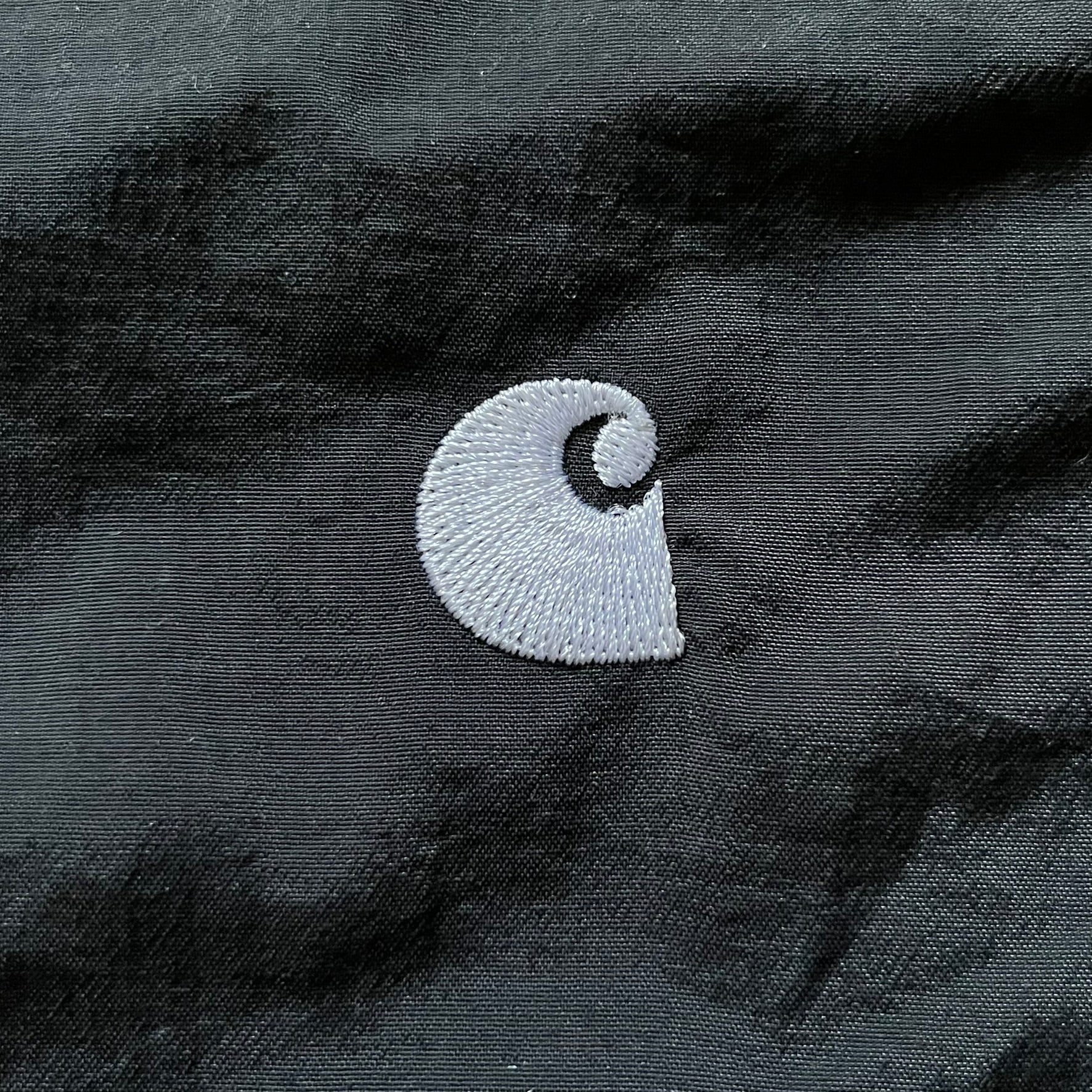 Carhartt WIP Gray Field Windbreaker featuring a dynamic two-tone design split diagonally across the body in light and dark gray. Crafted from durable nylon and polyester layers, it includes a small white Carhartt logo on the chest and large diagonal Carhartt embroidery on the back.