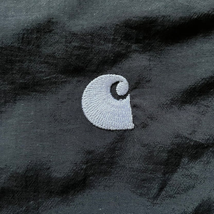 Carhartt WIP Gray Field Windbreaker featuring a dynamic two-tone design split diagonally across the body in light and dark gray. Crafted from durable nylon and polyester layers, it includes a small white Carhartt logo on the chest and large diagonal Carhartt embroidery on the back.