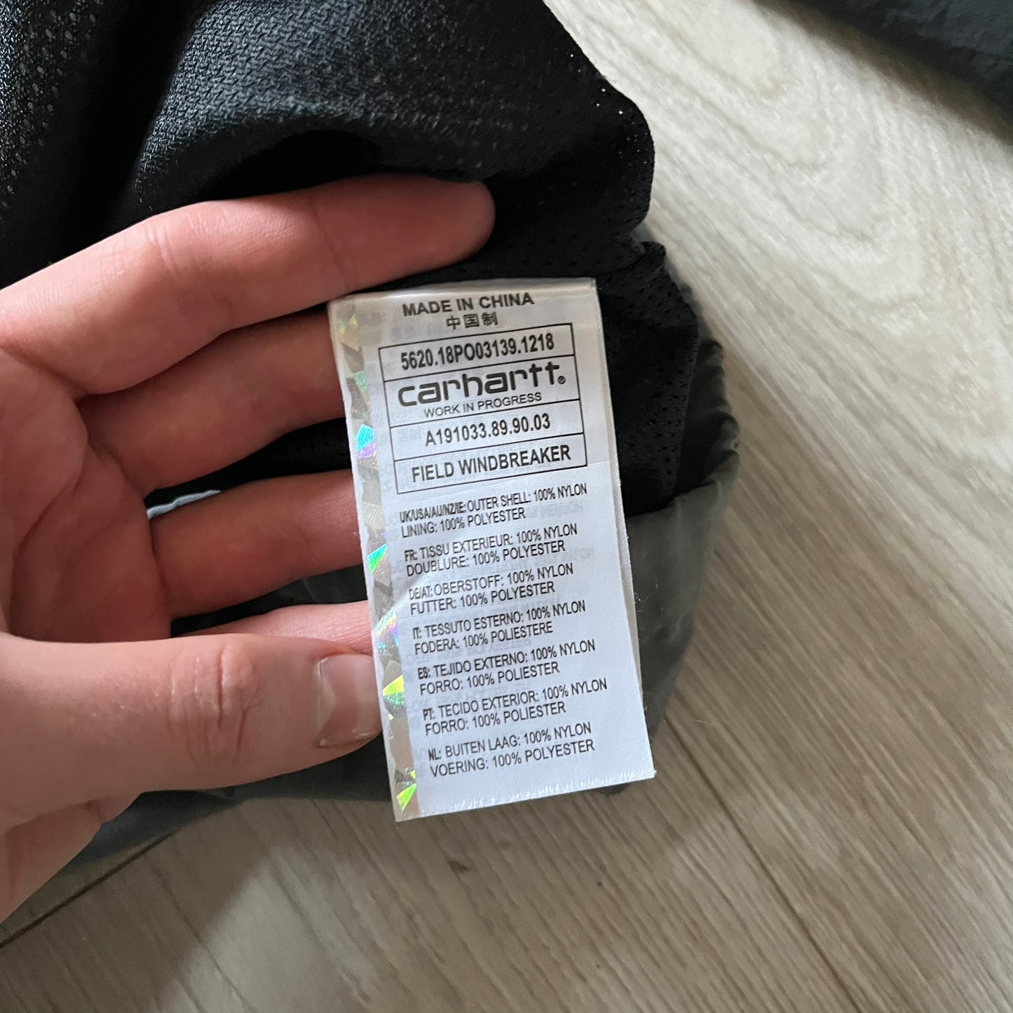 Carhartt WIP Gray Field Windbreaker featuring a dynamic two-tone design split diagonally across the body in light and dark gray. Crafted from durable nylon and polyester layers, it includes a small white Carhartt logo on the chest and large diagonal Carhartt embroidery on the back.