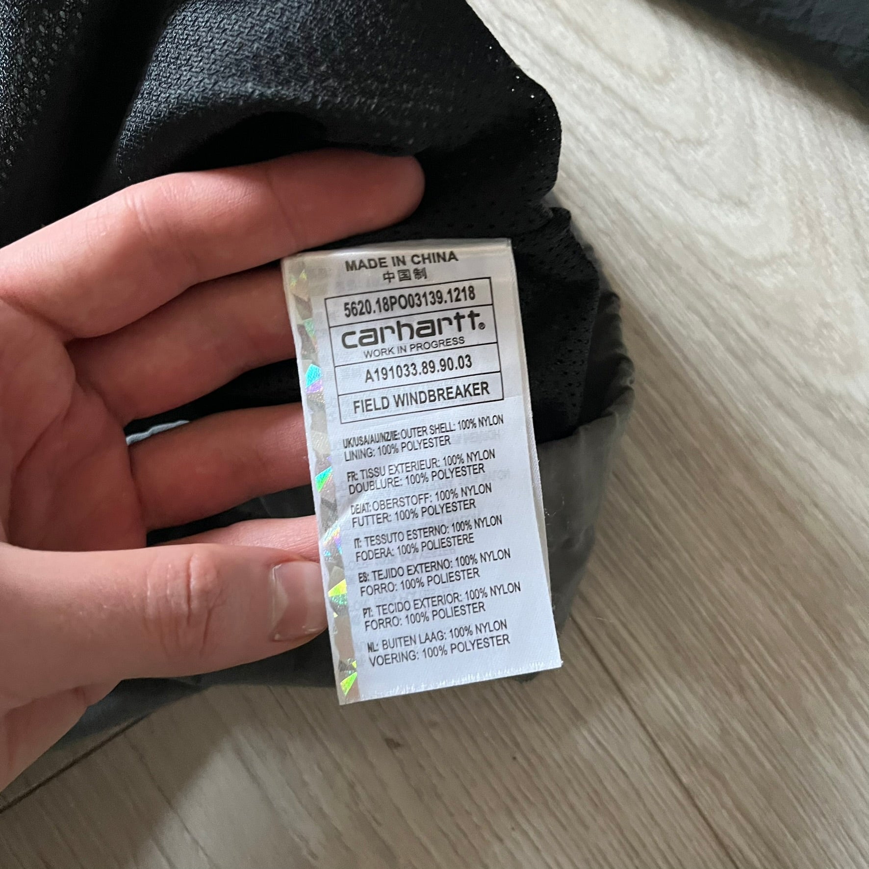 Carhartt WIP Gray Field Windbreaker featuring a dynamic two-tone design split diagonally across the body in light and dark gray. Crafted from durable nylon and polyester layers, it includes a small white Carhartt logo on the chest and large diagonal Carhartt embroidery on the back.