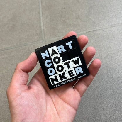 Cartoon Network 1999 Logo Puzzle is a handheld sliding tile puzzle featuring the classic Cartoon Network logo. The movable square tiles each display a single black or white letter, allowing the logo to be rearranged by sliding the pieces into place. Official 1999 licensing is printed on the bottom of the puzzle frame.