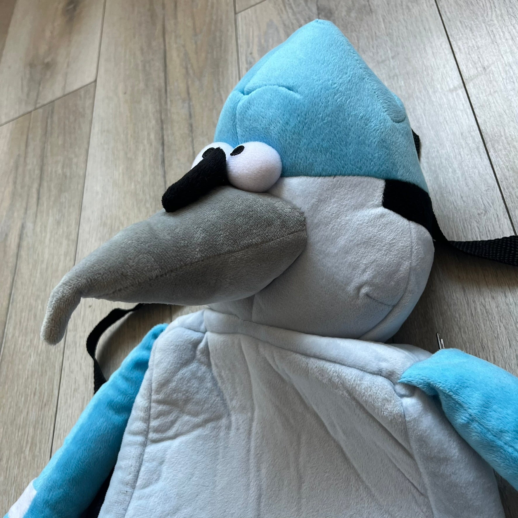 Cartoon Network Regular Show Mordecai 2016 Backpack is a full-body backpack featuring Mordecai with movable arms and legs. The straps attach from top to bottom, and the design shows his blue and light blue coloring, black head markings, striped wings, and tail feathers. The backpack replicates Mordecai’s animated appearance, including his crested head feathers and grey striped legs.