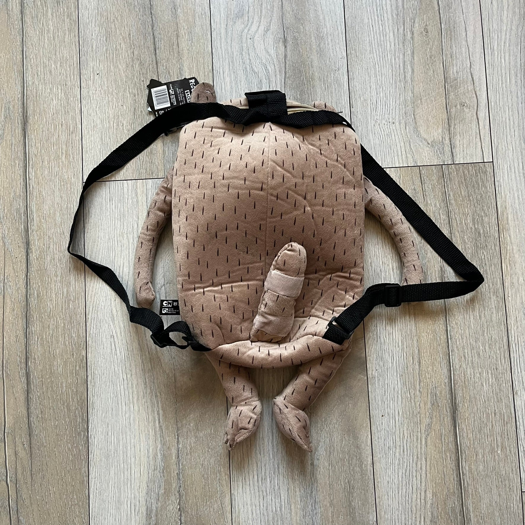 Cartoon Network Regular Show Rigby 2016 Backpack is a character-shaped backpack designed as Rigby from the animated series Regular Show. The bag features a full plush body construction with movable arms, legs, and mouth, while the eyes and mouth are finished with embroidered detailing. Adjustable straps are attached from the top to the lower back of the character, allowing it to be worn as a standard backpack. The design follows Rigby’s appearance with brown fur tones, dark raccoon-style eye mask markings, 