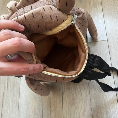 Cartoon Network Regular Show Rigby 2016 Backpack is a character-shaped backpack designed as Rigby from the animated series Regular Show. The bag features a full plush body construction with movable arms, legs, and mouth, while the eyes and mouth are finished with embroidered detailing. Adjustable straps are attached from the top to the lower back of the character, allowing it to be worn as a standard backpack. The design follows Rigby’s appearance with brown fur tones, dark raccoon-style eye mask markings, 