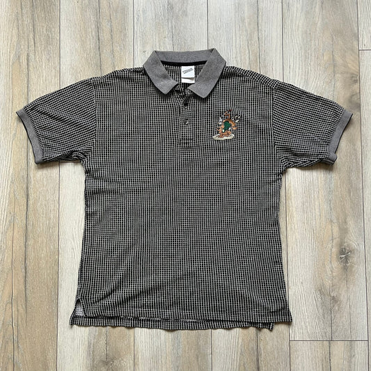 Cartoon Network Scooby-Doo 1999 Golf Polo is a black polo shirt featuring a grid pattern of thin white lines forming small squares across the fabric. The left chest displays an embroidered graphic of Scooby-Doo in a golf outfit digging in sand. The neck tag includes Warner Bros. and Cartoon Network 1999 licensing.
