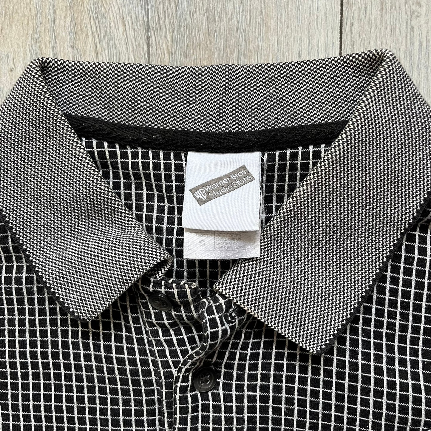 Cartoon Network Scooby-Doo 1999 Golf Polo is a black polo shirt featuring a grid pattern of thin white lines forming small squares across the fabric. The left chest displays an embroidered graphic of Scooby-Doo in a golf outfit digging in sand. The neck tag includes Warner Bros. and Cartoon Network 1999 licensing.