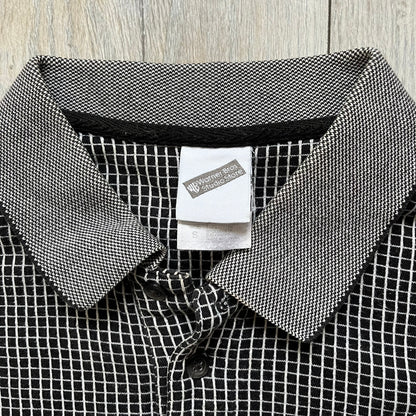 Cartoon Network Scooby-Doo 1999 Golf Polo is a black polo shirt featuring a grid pattern of thin white lines forming small squares across the fabric. The left chest displays an embroidered graphic of Scooby-Doo in a golf outfit digging in sand. The neck tag includes Warner Bros. and Cartoon Network 1999 licensing.