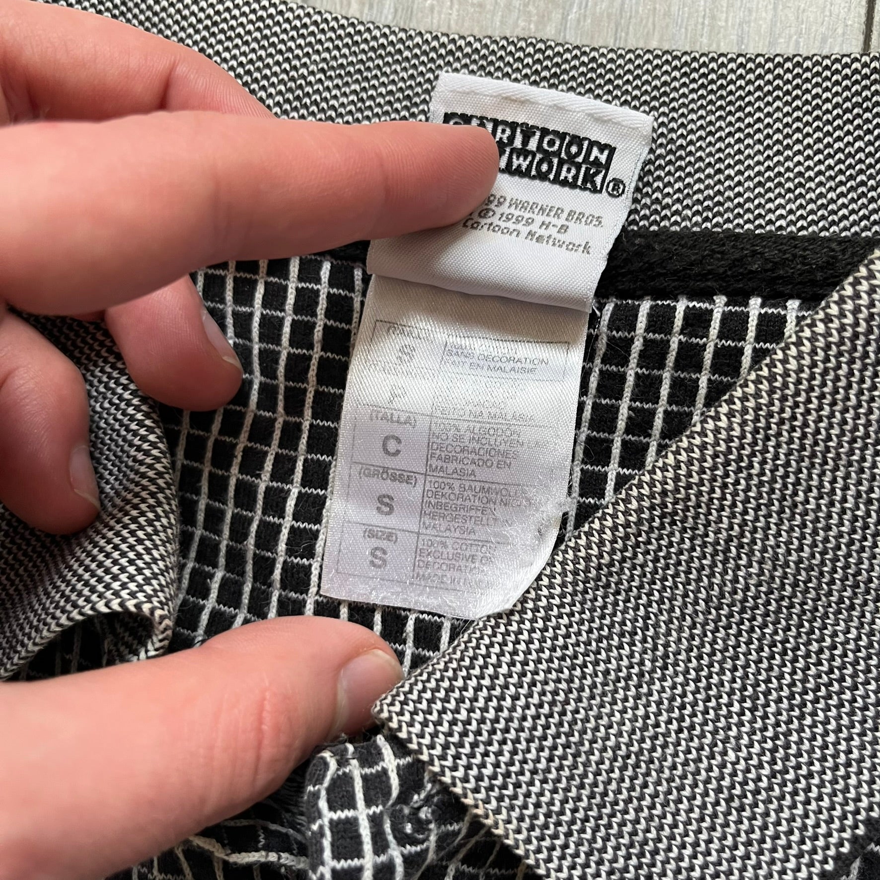 Cartoon Network Scooby-Doo 1999 Golf Polo is a black polo shirt featuring a grid pattern of thin white lines forming small squares across the fabric. The left chest displays an embroidered graphic of Scooby-Doo in a golf outfit digging in sand. The neck tag includes Warner Bros. and Cartoon Network 1999 licensing.