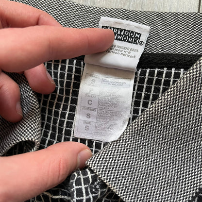 Cartoon Network Scooby-Doo 1999 Golf Polo is a black polo shirt featuring a grid pattern of thin white lines forming small squares across the fabric. The left chest displays an embroidered graphic of Scooby-Doo in a golf outfit digging in sand. The neck tag includes Warner Bros. and Cartoon Network 1999 licensing.