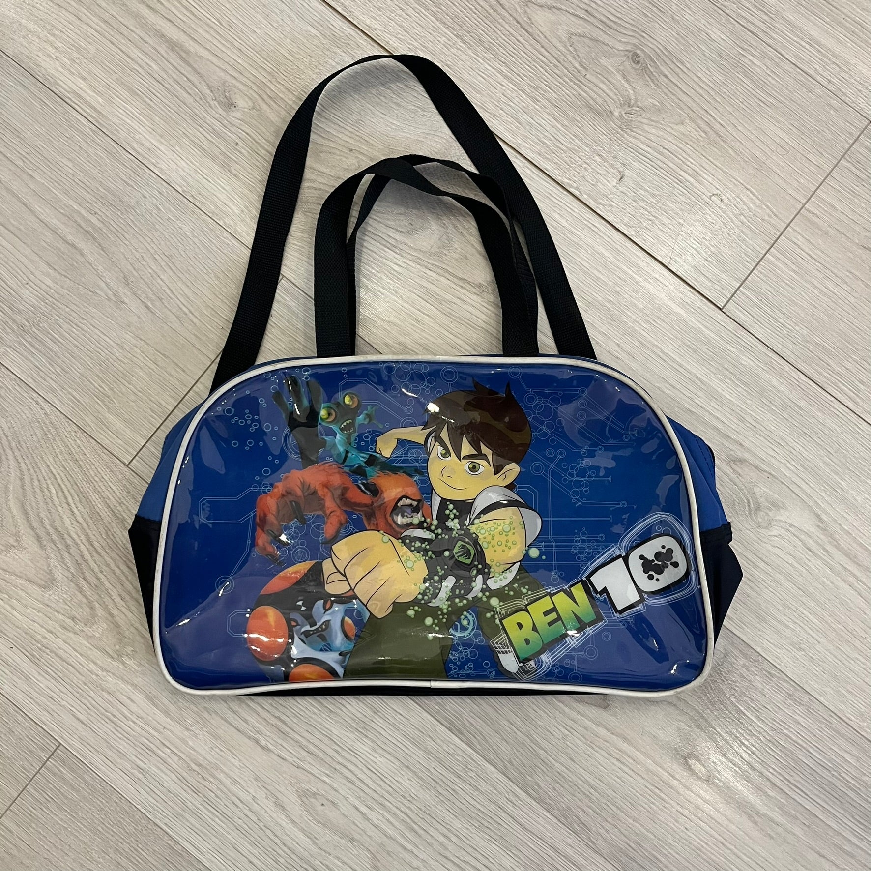 Blue Cartoon Network “Ben 10” handbag with black straps. Features a front graphic of Ben 10 with several of his evolve forms and the Ben 10 logo on the bottom right. Includes an internal Cartoon Network tag marked S10 for the 2010 season.
