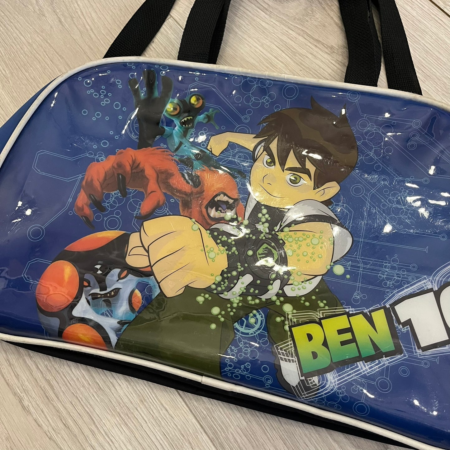 Blue Cartoon Network “Ben 10” handbag with black straps. Features a front graphic of Ben 10 with several of his evolve forms and the Ben 10 logo on the bottom right. Includes an internal Cartoon Network tag marked S10 for the 2010 season.