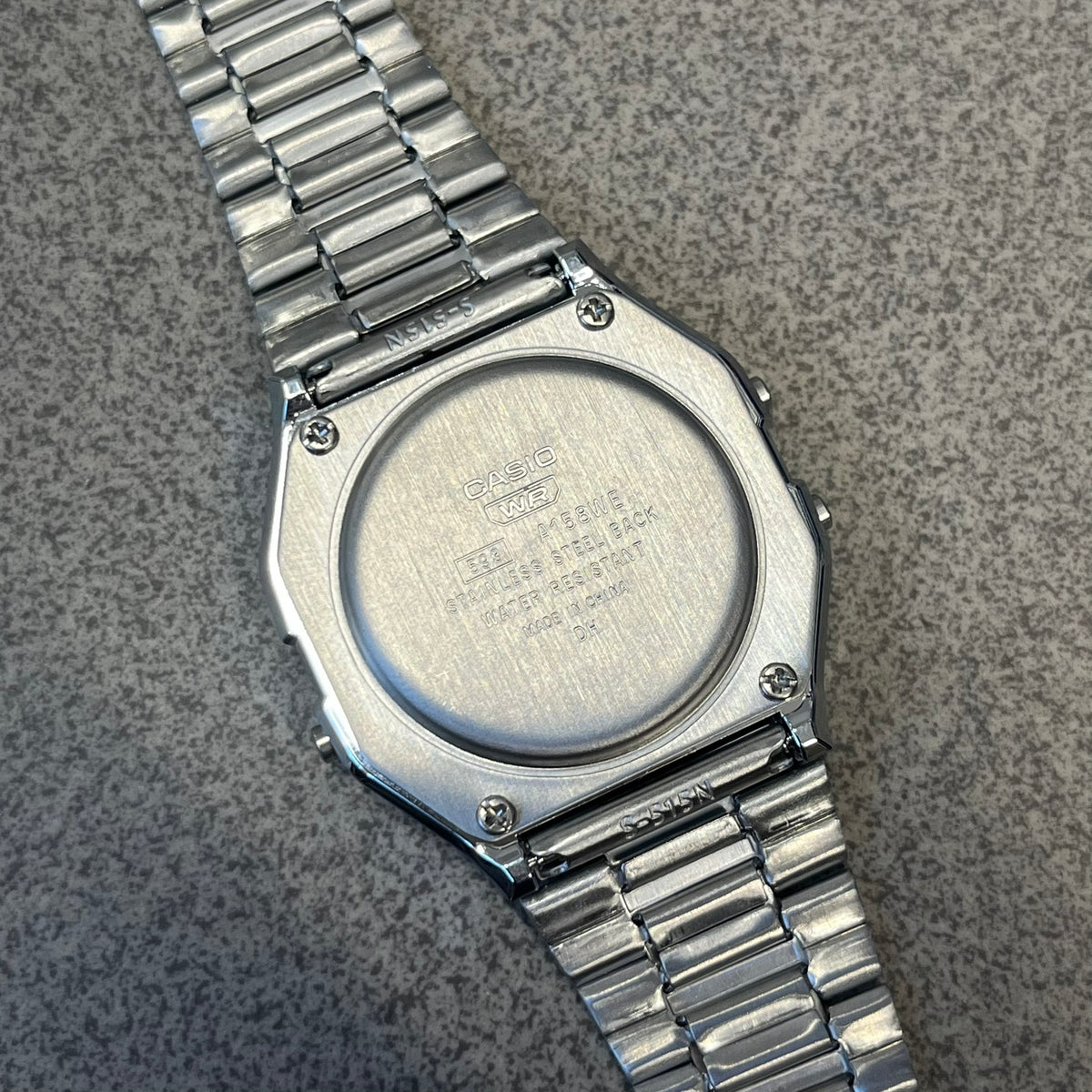 Custom Casio A158 "Double Holo" Silver Digital Watch (A158WEA-7EF) is a custom Casio digital watch with a Double Holo (Stars and normal holo) filter over the square resin glass screen and a stainless steel band with an adjustable clasp, compatible with wrist sizes from 150 to 205 mm. It has a 1/100-second stopwatch, a daily alarm, an hourly time signal, an auto-calendar, a 12/24-hour format, a green LED light, and water resistance.