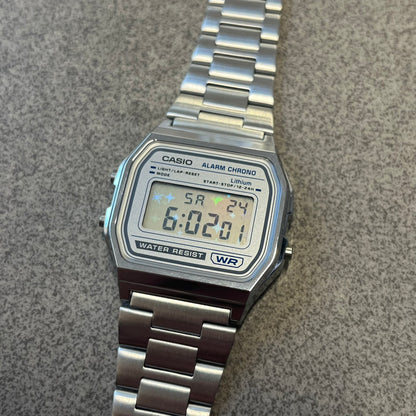 Custom Casio A158 "Double Holo" Silver Digital Watch (A158WEA-7EF) is a custom Casio digital watch with a Double Holo (Stars and normal holo) filter over the square resin glass screen and a stainless steel band with an adjustable clasp, compatible with wrist sizes from 150 to 205 mm. It has a 1/100-second stopwatch, a daily alarm, an hourly time signal, an auto-calendar, a 12/24-hour format, a green LED light, and water resistance.