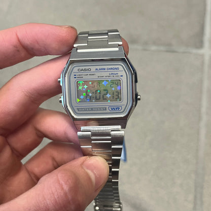 Custom Casio A158 "Double Holo" Silver Digital Watch (A158WEA-7EF) is a custom Casio digital watch with a Double Holo (Stars and normal holo) filter over the square resin glass screen and a stainless steel band with an adjustable clasp, compatible with wrist sizes from 150 to 205 mm. It has a 1/100-second stopwatch, a daily alarm, an hourly time signal, an auto-calendar, a 12/24-hour format, a green LED light, and water resistance.