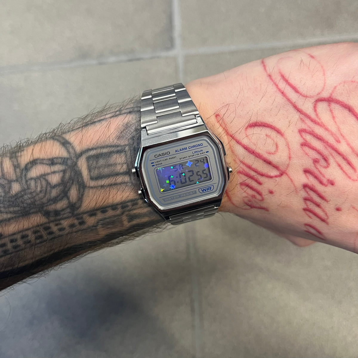 Custom Casio A158 "Double Holo" Silver Digital Watch (A158WEA-7EF) is a custom Casio digital watch with a Double Holo (Stars and normal holo) filter over the square resin glass screen and a stainless steel band with an adjustable clasp, compatible with wrist sizes from 150 to 205 mm. It has a 1/100-second stopwatch, a daily alarm, an hourly time signal, an auto-calendar, a 12/24-hour format, a green LED light, and water resistance.
