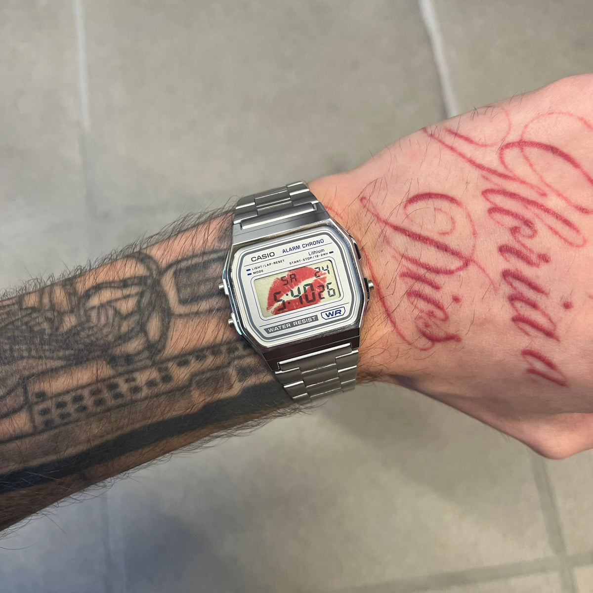 Custom Casio A158 “Kiss Me” Red &amp; Silver Digital Watch (A158WEA-7EF) is a custom Casio digital watch with a red lips filter over the square resin glass screen and a stainless steel band with an adjustable clasp, compatible with wrist sizes from 150 to 205 mm. It has a 1/100-second stopwatch, a daily alarm, an hourly time signal, an auto-calendar, a 12/24-hour format, a green LED light, and water resistance.