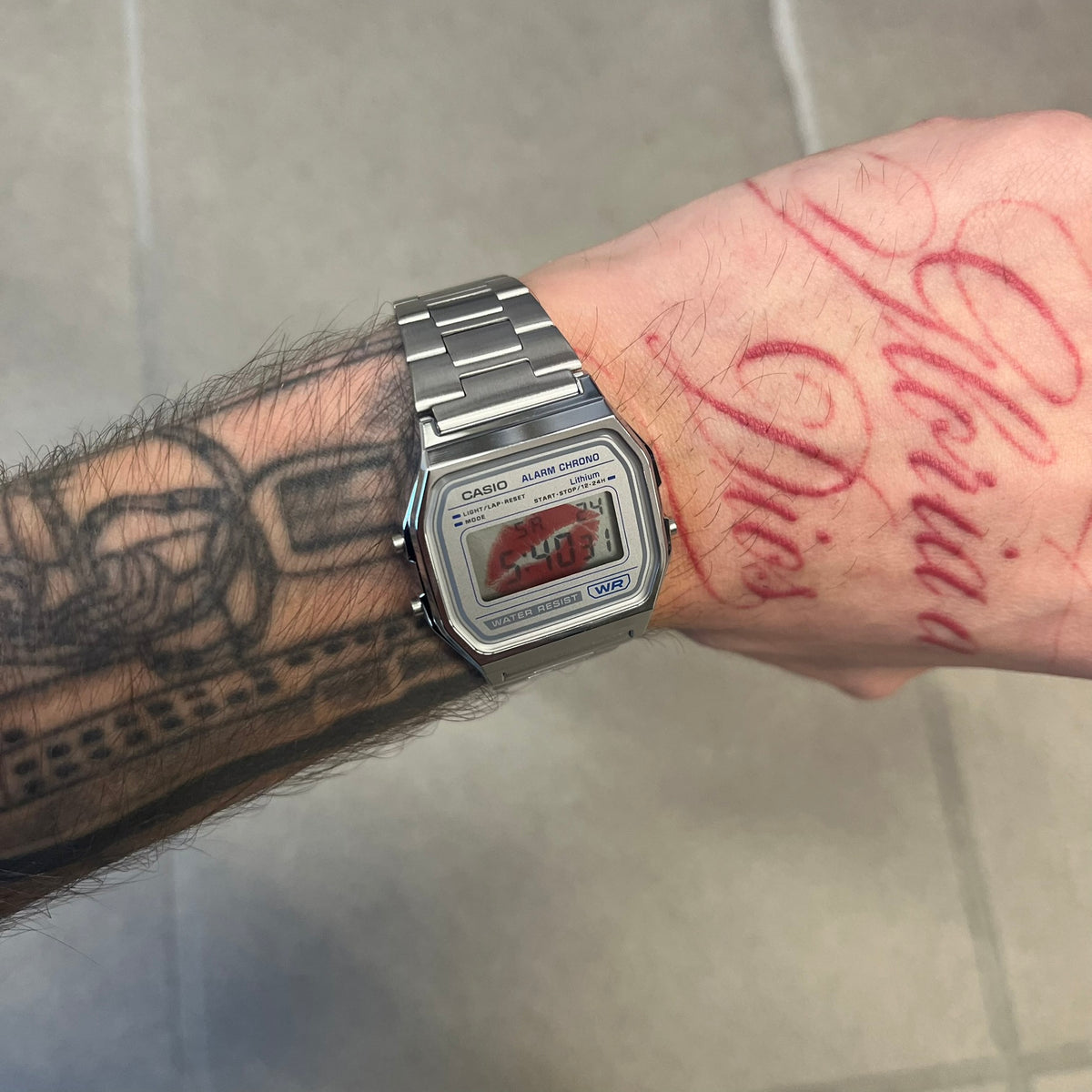 Custom Casio A158 “Kiss Me” Red &amp; Silver Digital Watch (A158WEA-7EF) is a custom Casio digital watch with a red lips filter over the square resin glass screen and a stainless steel band with an adjustable clasp, compatible with wrist sizes from 150 to 205 mm. It has a 1/100-second stopwatch, a daily alarm, an hourly time signal, an auto-calendar, a 12/24-hour format, a green LED light, and water resistance.