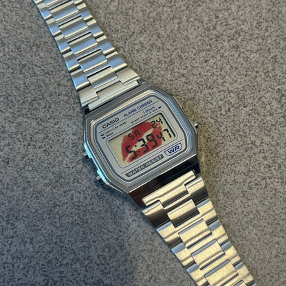 Custom Casio A158 “Kiss Me” Red &amp; Silver Digital Watch (A158WEA-7EF) is a custom Casio digital watch with a red lips filter over the square resin glass screen and a stainless steel band with an adjustable clasp, compatible with wrist sizes from 150 to 205 mm. It has a 1/100-second stopwatch, a daily alarm, an hourly time signal, an auto-calendar, a 12/24-hour format, a green LED light, and water resistance.