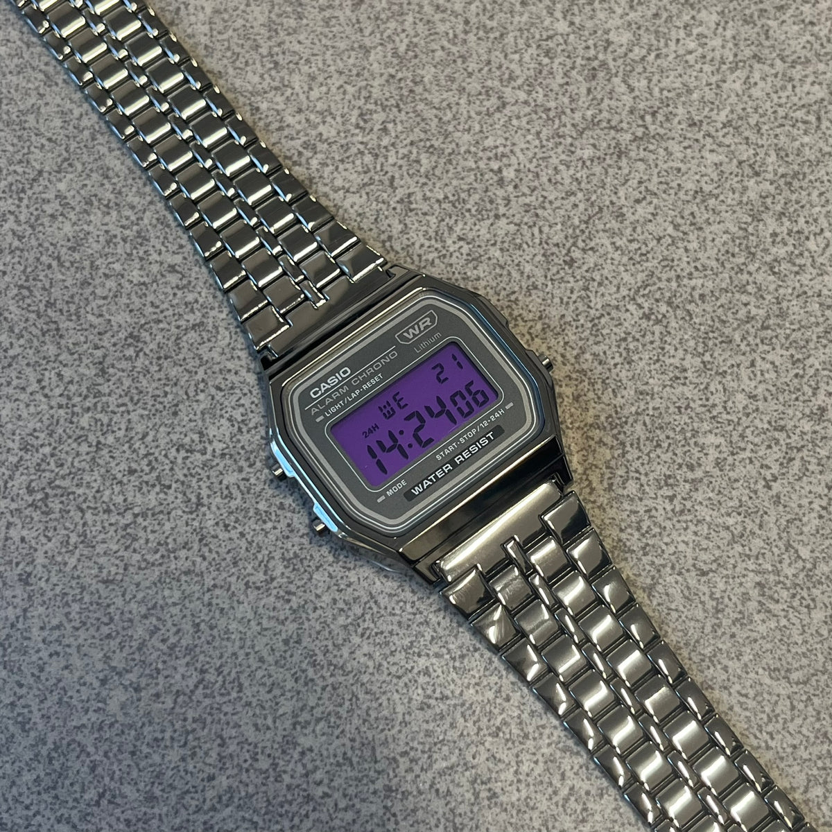 Custom Casio A158 "Royal Purple" Black &amp; Purple Digital Watch is a watch with a purple filter over the square screen and a grey ion-plated stainless steel band with an adjustable clasp. The case comes with a resin glass and a resin and black chrome-plated case and bezel. It has a 1/100-second stopwatch, a daily alarm, an hourly time signal, an auto-calendar, a 12/24-hour format, a green LED light, and water resistance.