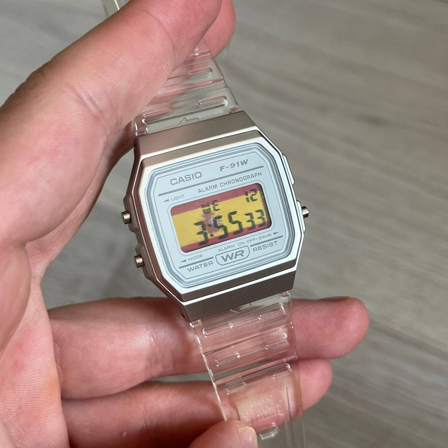 Custom Casio F-91W Clear/Transparent digital watch featuring a Spanish Flag filter screen. Slim 8.5 mm profile, lightweight 21 g build and flexible bio-based resin band ensure lasting comfort. Includes alarm, stopwatch, and microlight function for everyday functionality.